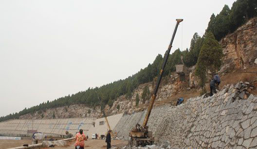 孔子诞生地曲阜市尼山水库护坡工程紧张施工 位于曲阜市尼山风景区的尼山水库北岸溢洪道上游北面曲尼旅游公路路侧的山体护坡工程正在紧张施工。 尼山水库是上世纪五十年代修建的全国大型水库,设计兴利库容1.28亿立方,是曲阜市战略水资源重地,也是孔子诞生地尼山风景区的著名风景点。位于尼山水库大坝北岸溢洪道东侧、曲尼旅游公路北面的尼山山体,每年汛期都会发生坍塌滑坡现象,给尼山水库造成隐患,同时也给到尼山风景区旅游的游客造成人身安全隐患。为此,尼山水库管理局经省、市有关部门立项批复,从今年10月开始组织施工人员进行水